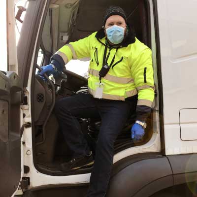 Delivery driver stepping down from the cab, wearing a mask and gloves for COVID-19.